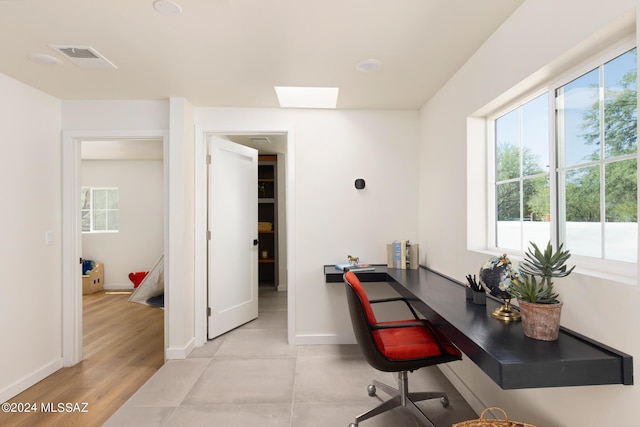 office area featuring light wood-type flooring, a skylight, visible vents, and baseboards