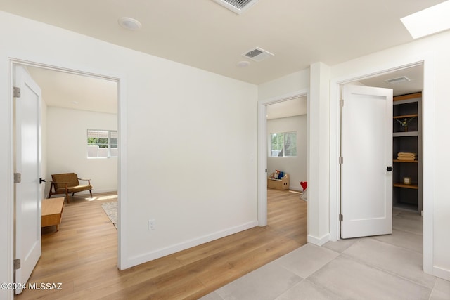 hallway with light wood-type flooring, a skylight, baseboards, and visible vents