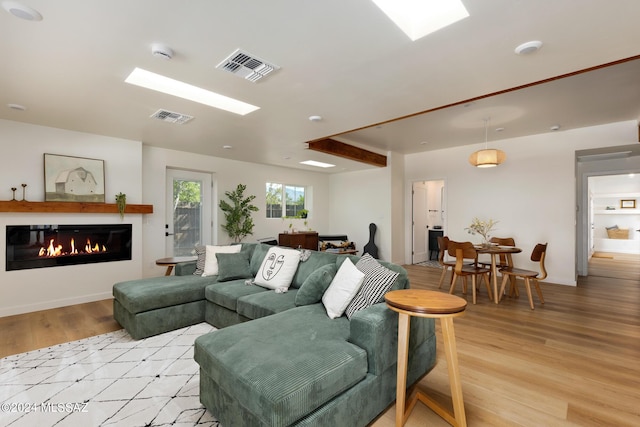 living room featuring light wood-type flooring, baseboards, visible vents, and a glass covered fireplace