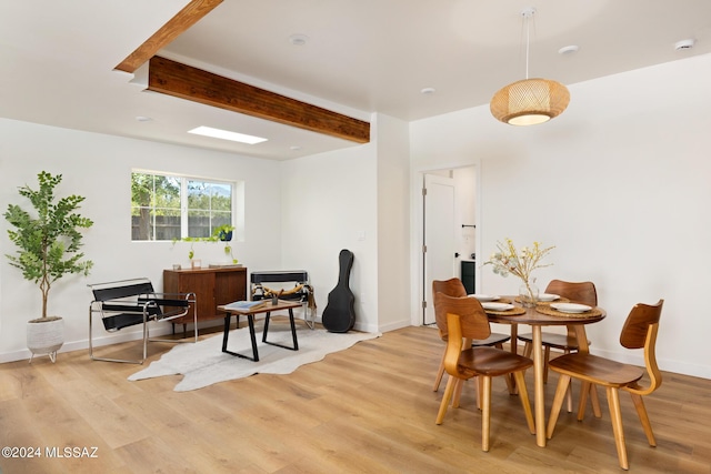 dining area featuring light wood-style flooring, baseboards, and beam ceiling