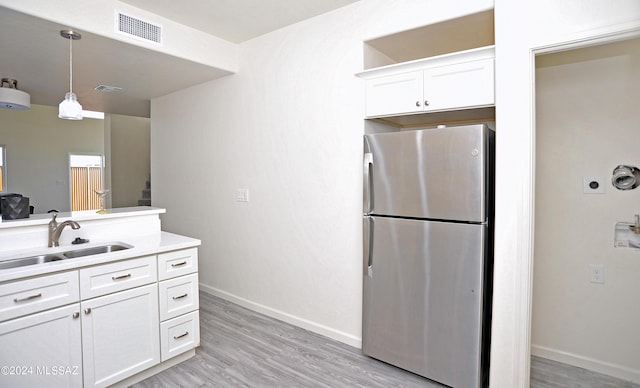 kitchen featuring pendant lighting, white cabinets, sink, stainless steel fridge, and light hardwood / wood-style floors