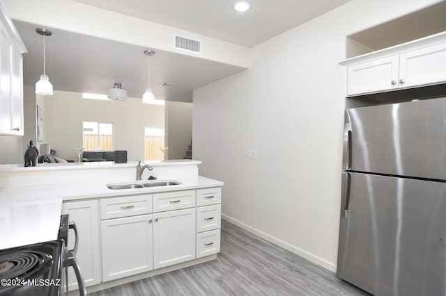 kitchen with pendant lighting, white cabinets, sink, and stainless steel refrigerator