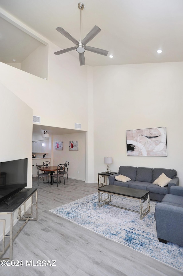 living room with ceiling fan, light hardwood / wood-style floors, and a high ceiling