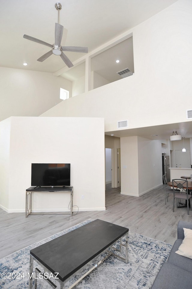 living room with ceiling fan, a towering ceiling, and wood-type flooring