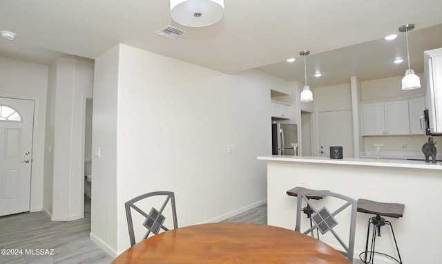 kitchen featuring stainless steel refrigerator, hanging light fixtures, kitchen peninsula, light hardwood / wood-style floors, and white cabinets