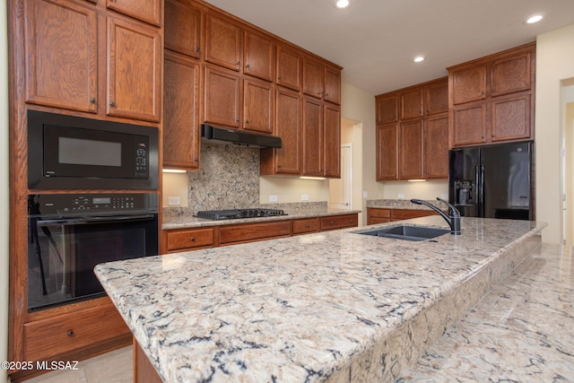 kitchen with black appliances, a center island with sink, light stone countertops, and sink