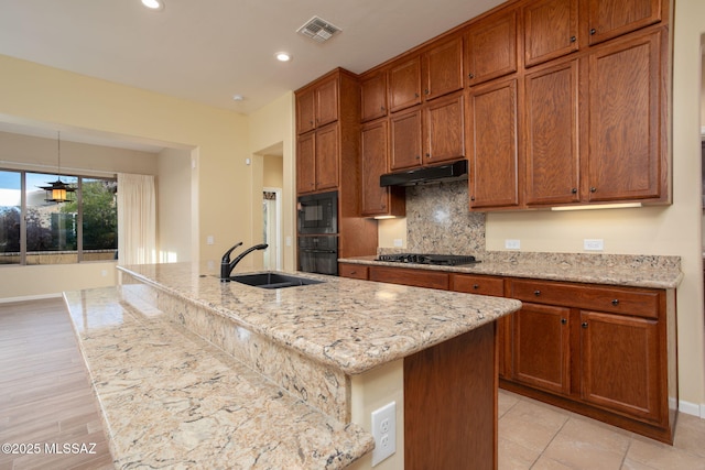 kitchen featuring light stone countertops, backsplash, sink, black appliances, and an island with sink