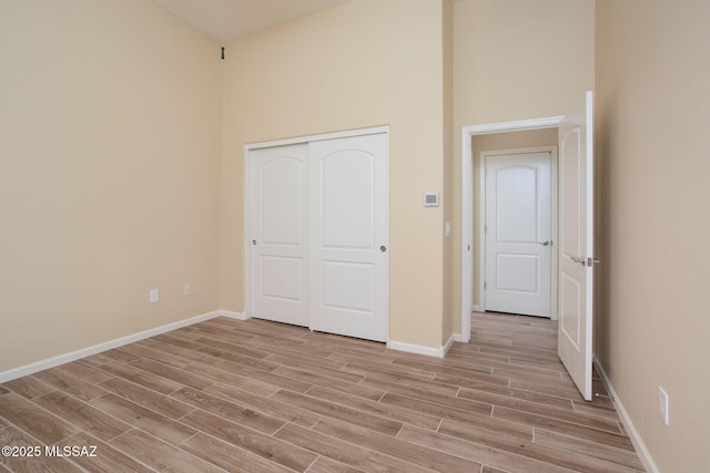 unfurnished bedroom featuring a high ceiling, light hardwood / wood-style floors, and a closet