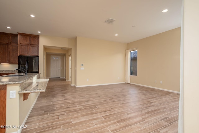 kitchen featuring light stone countertops, light wood-type flooring, black fridge, sink, and a breakfast bar area