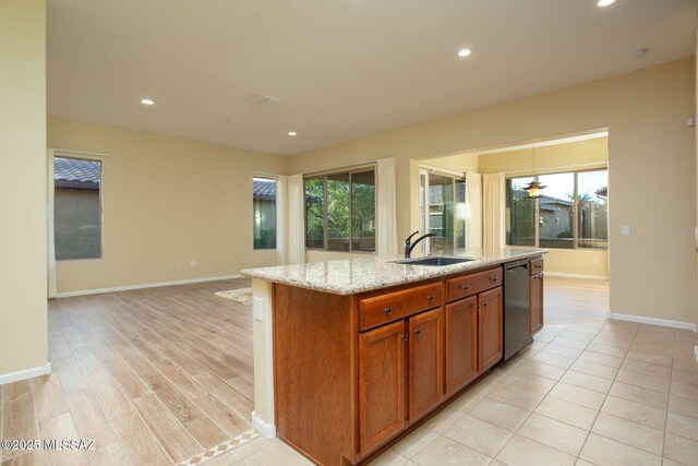 kitchen with ceiling fan, sink, dishwasher, light stone counters, and a kitchen island with sink