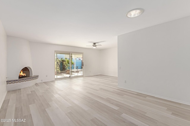 unfurnished living room with ceiling fan, a large fireplace, and light hardwood / wood-style floors