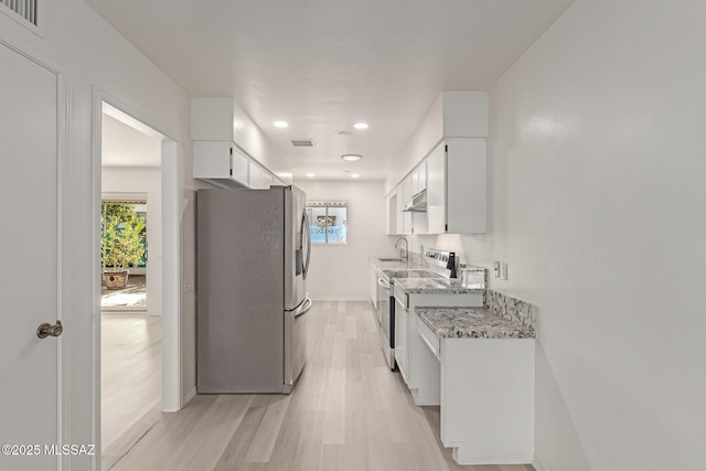 kitchen with light stone countertops, light wood-type flooring, stainless steel appliances, sink, and white cabinets