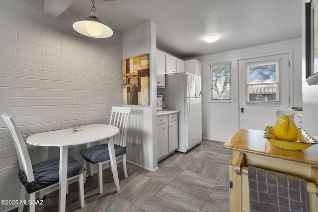 kitchen featuring white cabinetry, brick wall, decorative light fixtures, and white refrigerator