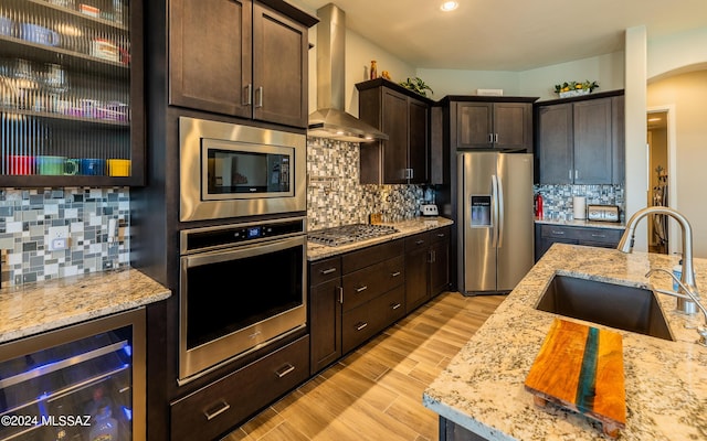 kitchen featuring wine cooler, wall chimney exhaust hood, dark brown cabinetry, sink, and appliances with stainless steel finishes