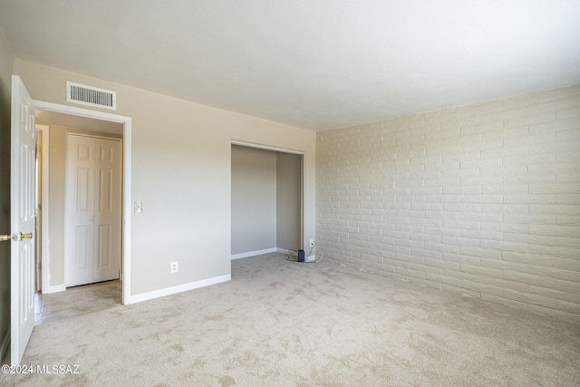 unfurnished bedroom featuring light carpet, brick wall, and a closet