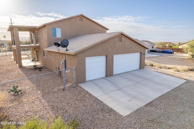 view of side of home featuring stucco siding, a gate, fence, concrete driveway, and a garage