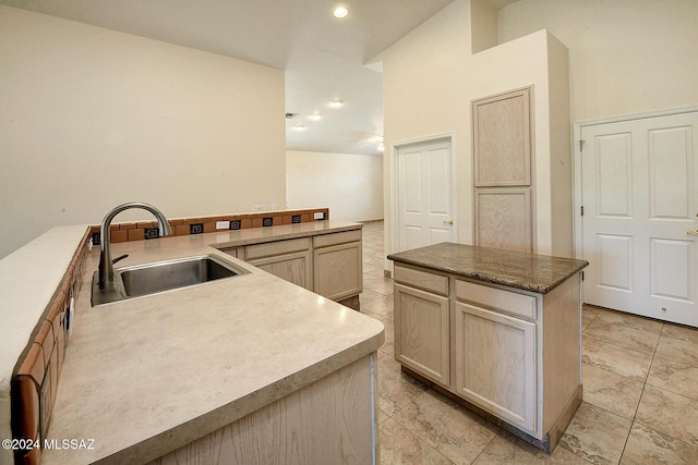 kitchen with light brown cabinetry, sink, a kitchen island, and high vaulted ceiling