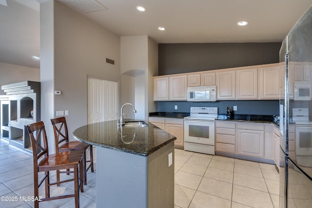 kitchen with dark stone counters, white appliances, a kitchen island with sink, sink, and light tile patterned flooring