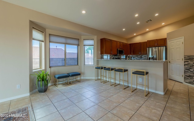 kitchen with stainless steel appliances, tasteful backsplash, kitchen peninsula, vaulted ceiling, and light tile patterned floors