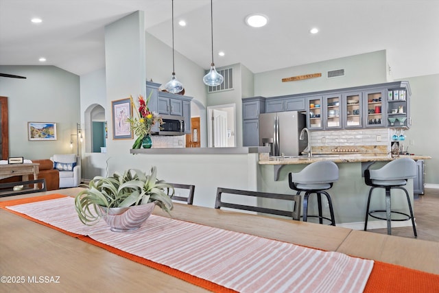 kitchen with arched walkways, a breakfast bar, stainless steel appliances, glass insert cabinets, and a peninsula