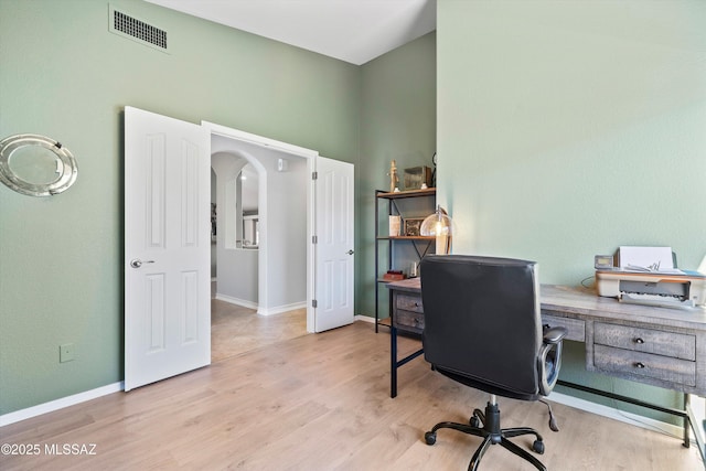 home office with arched walkways, wood finished floors, visible vents, and baseboards