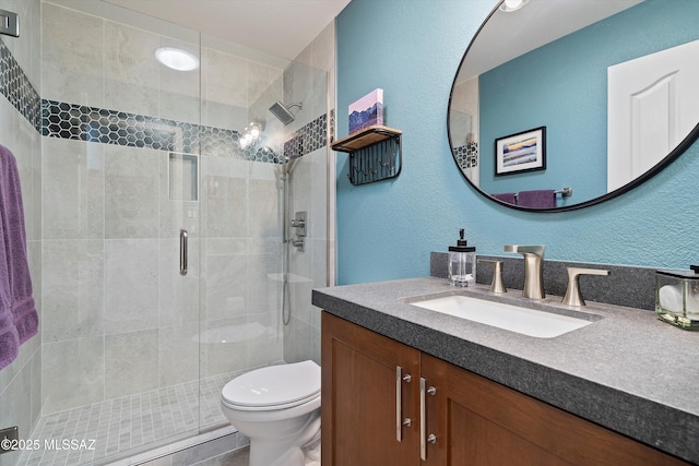 full bathroom with toilet, a stall shower, a textured wall, and vanity