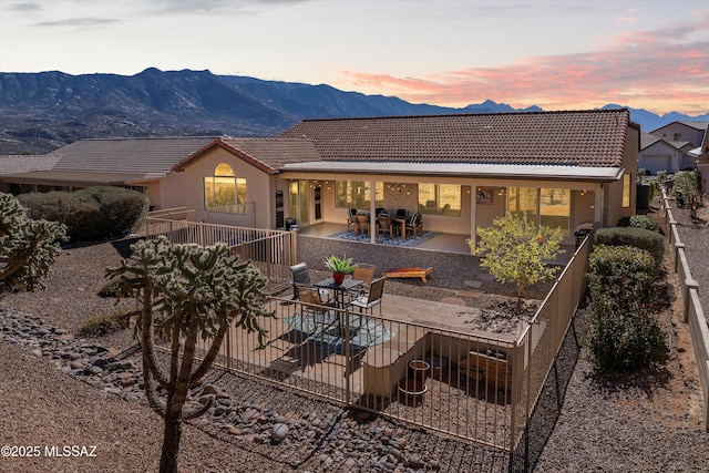 back of house at dusk featuring a patio area, a tile roof, a mountain view, and stucco siding