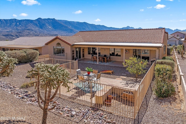 rear view of house with a tiled roof, fence, a patio area, a mountain view, and stucco siding