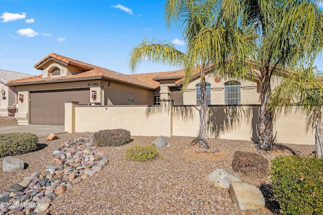 mediterranean / spanish house with a tiled roof, a fenced front yard, an attached garage, and stucco siding