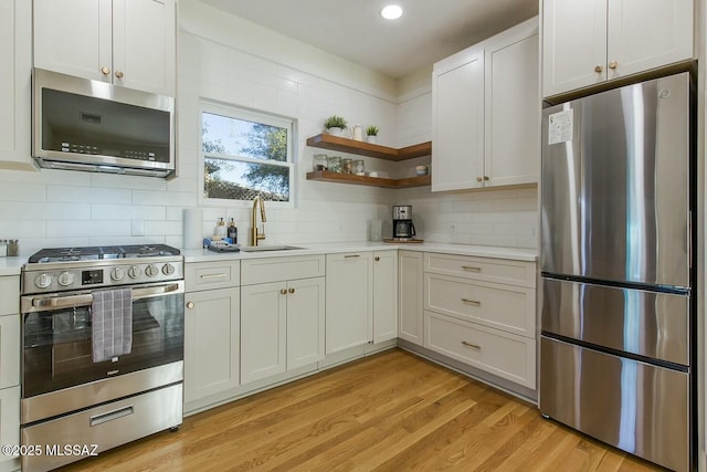 kitchen with sink, backsplash, light hardwood / wood-style floors, white cabinets, and appliances with stainless steel finishes