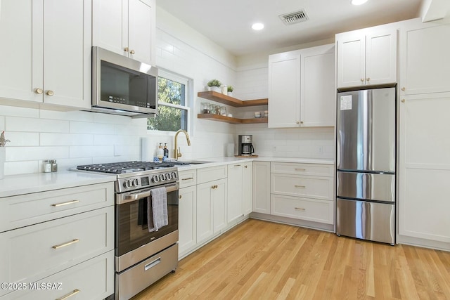 kitchen with white cabinetry, stainless steel appliances, and light hardwood / wood-style flooring