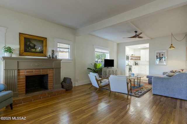 living room featuring ceiling fan, beam ceiling, wood-type flooring, and a brick fireplace