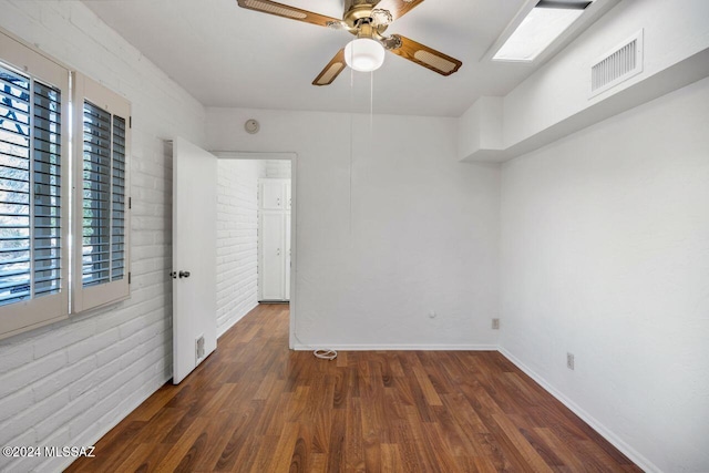 unfurnished room with a skylight, dark hardwood / wood-style floors, ceiling fan, and brick wall