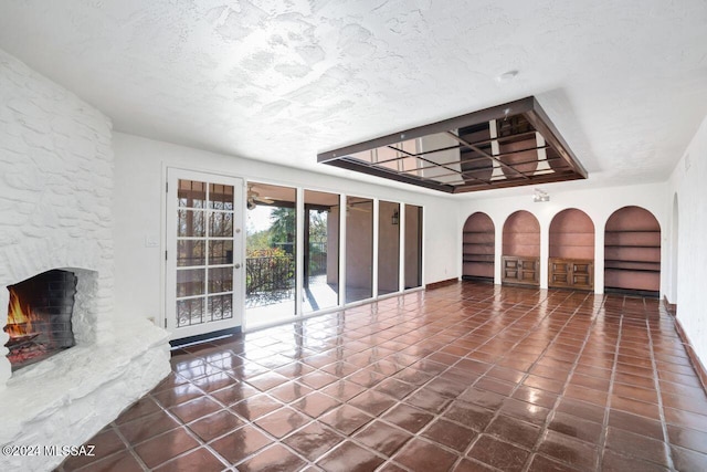 unfurnished living room with a textured ceiling, built in features, a fireplace, and dark tile patterned flooring