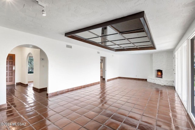 tiled empty room with a stone fireplace and a textured ceiling