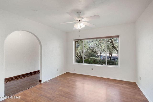 empty room with a ceiling fan, arched walkways, baseboards, and wood finished floors