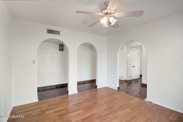 empty room featuring arched walkways, visible vents, a ceiling fan, and wood finished floors