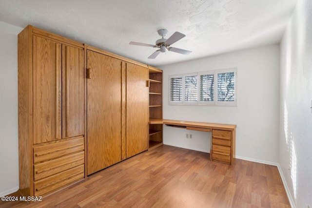 interior space with a textured ceiling, built in desk, light hardwood / wood-style floors, and ceiling fan