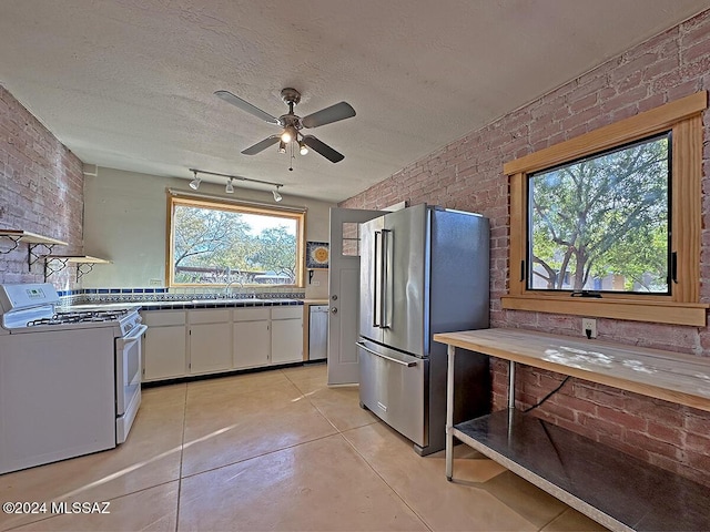 kitchen with appliances with stainless steel finishes, brick wall, a textured ceiling, light tile patterned floors, and white cabinets