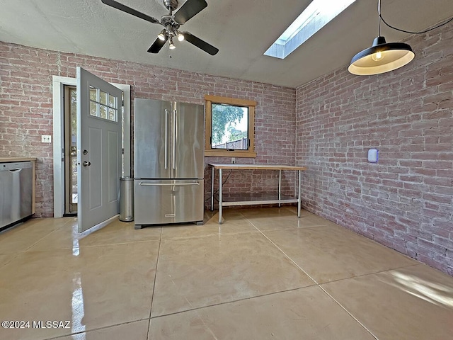 kitchen with ceiling fan, brick wall, appliances with stainless steel finishes, and a skylight