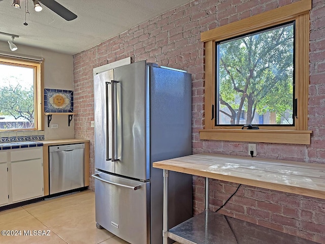 kitchen with white cabinets, sink, light tile patterned floors, appliances with stainless steel finishes, and brick wall