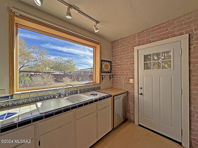 kitchen with white cabinetry, dishwasher, tile counters, sink, and brick wall