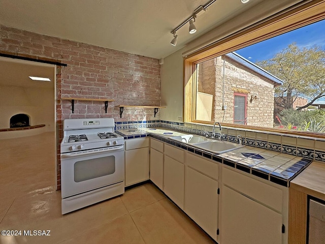 kitchen featuring sink, white range with gas stovetop, brick wall, tile countertops, and light tile patterned flooring