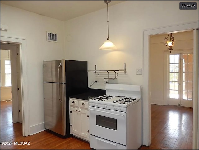 kitchen with wood-type flooring, hanging light fixtures, white gas range, white cabinetry, and stainless steel refrigerator