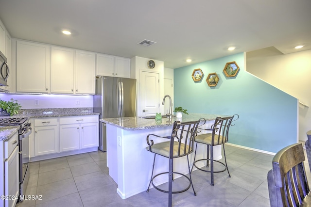 kitchen featuring a kitchen island with sink, white cabinets, light stone counters, and appliances with stainless steel finishes