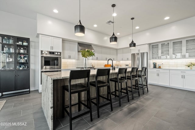 kitchen featuring a breakfast bar, a center island with sink, white cabinets, and hanging light fixtures