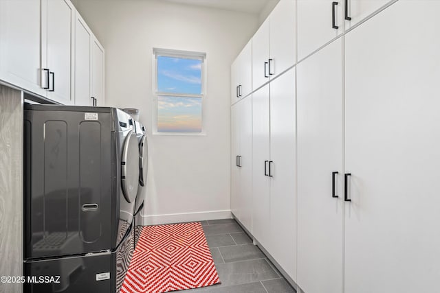 laundry room featuring washing machine and clothes dryer, dark tile patterned floors, and cabinets