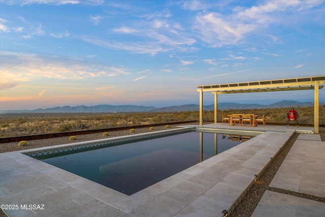 pool at dusk featuring a mountain view and a patio