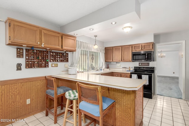 kitchen with black electric range oven, light tile patterned floors, decorative light fixtures, a kitchen bar, and kitchen peninsula