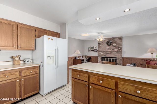 kitchen featuring ceiling fan, white fridge with ice dispenser, a brick fireplace, wood walls, and a textured ceiling